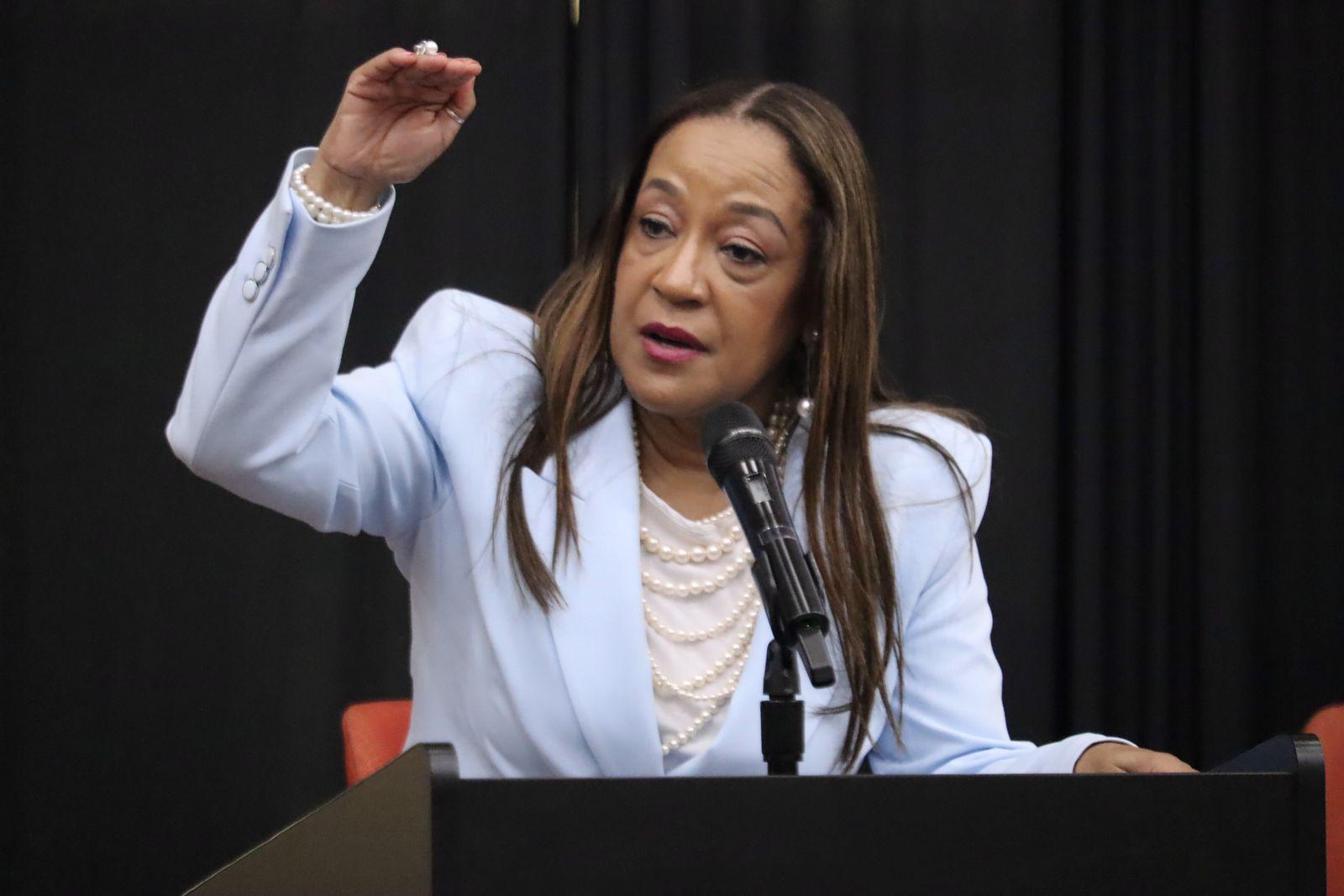 Dr. Carolyn Haliburton Carter speaking at a lectern with a microphone, one hand raised mid-gesture.