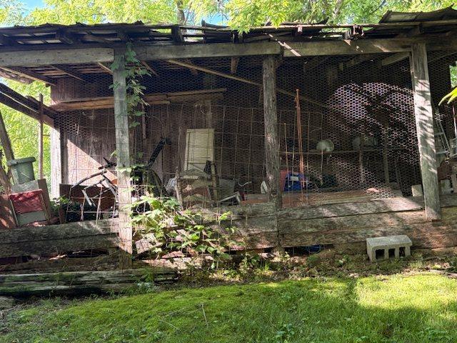 The remains of a timber outbuilding, roof partly collapsed and the structure overgrown, photographed in summer.